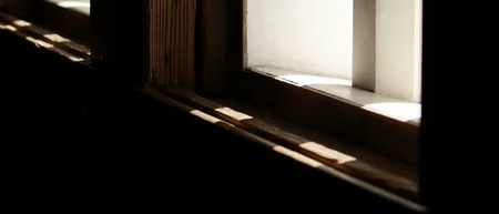 Sonnenlicht fällt durch ein schmales Fenster mit dunklem Holzrahmen