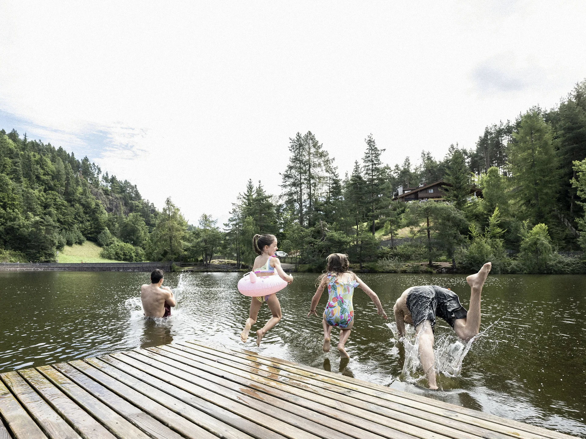 Urlaub am Ritten: die Insider-Tipps des Armonia Kinder und Erwachsene springen von einem Holzsteg in einen von Wald umgebenen See