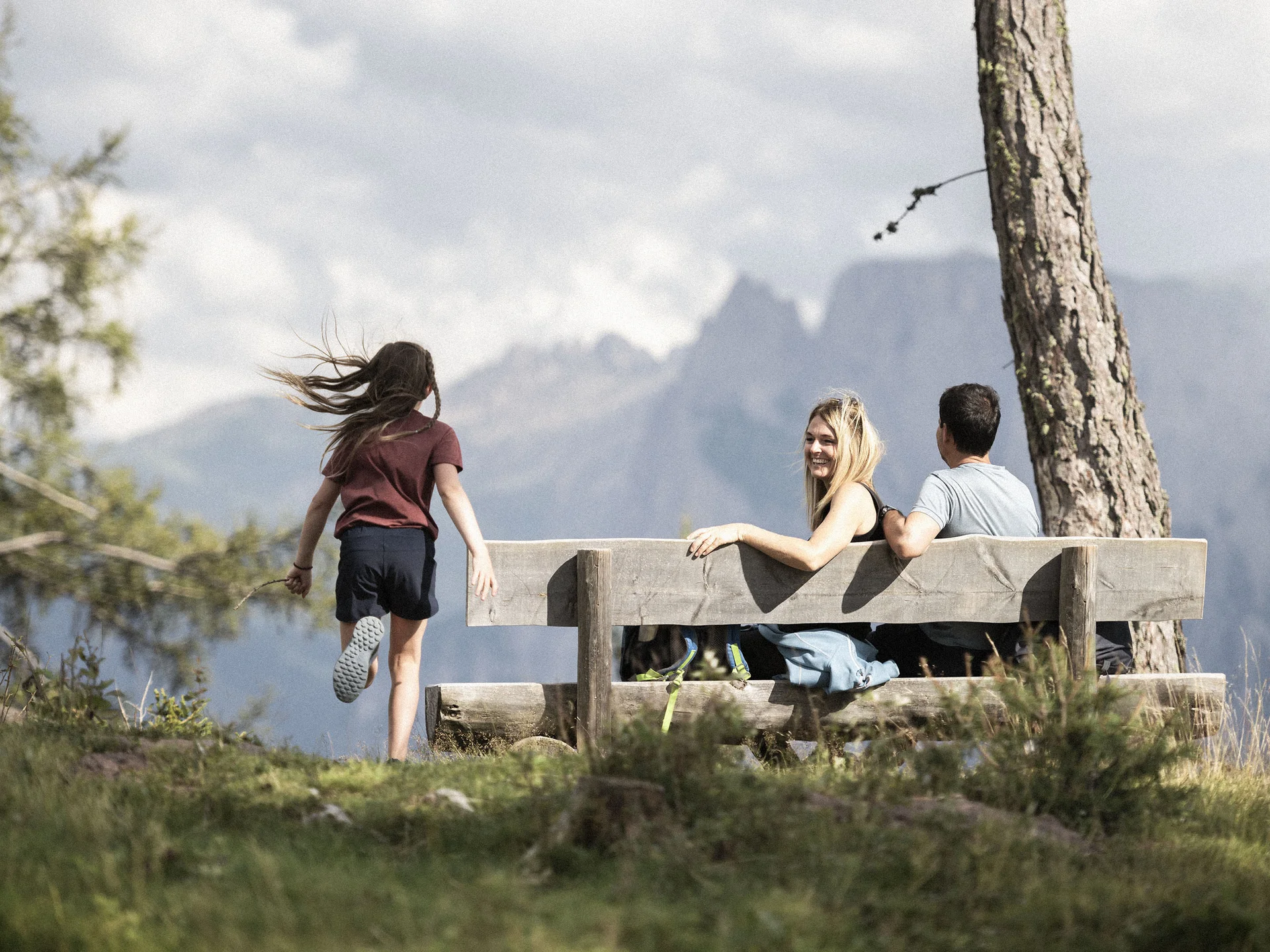 Urlaub am Ritten: die Insider-Tipps des Armonia Ein Mädchen läuft zu zwei Personen auf einer Holzbank mit Bergblick