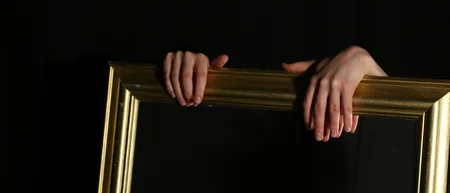 Hände halten einen goldenen Bilderrahmen vor schwarzem Hintergrund