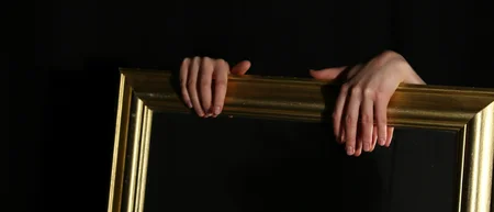 Hände halten einen goldenen Bilderrahmen vor schwarzem Hintergrund