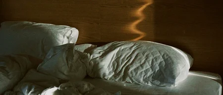 Sonnenlicht zeichnet eine geschwungene Spur auf das Holzkopfteil über einem ungemachten Bett