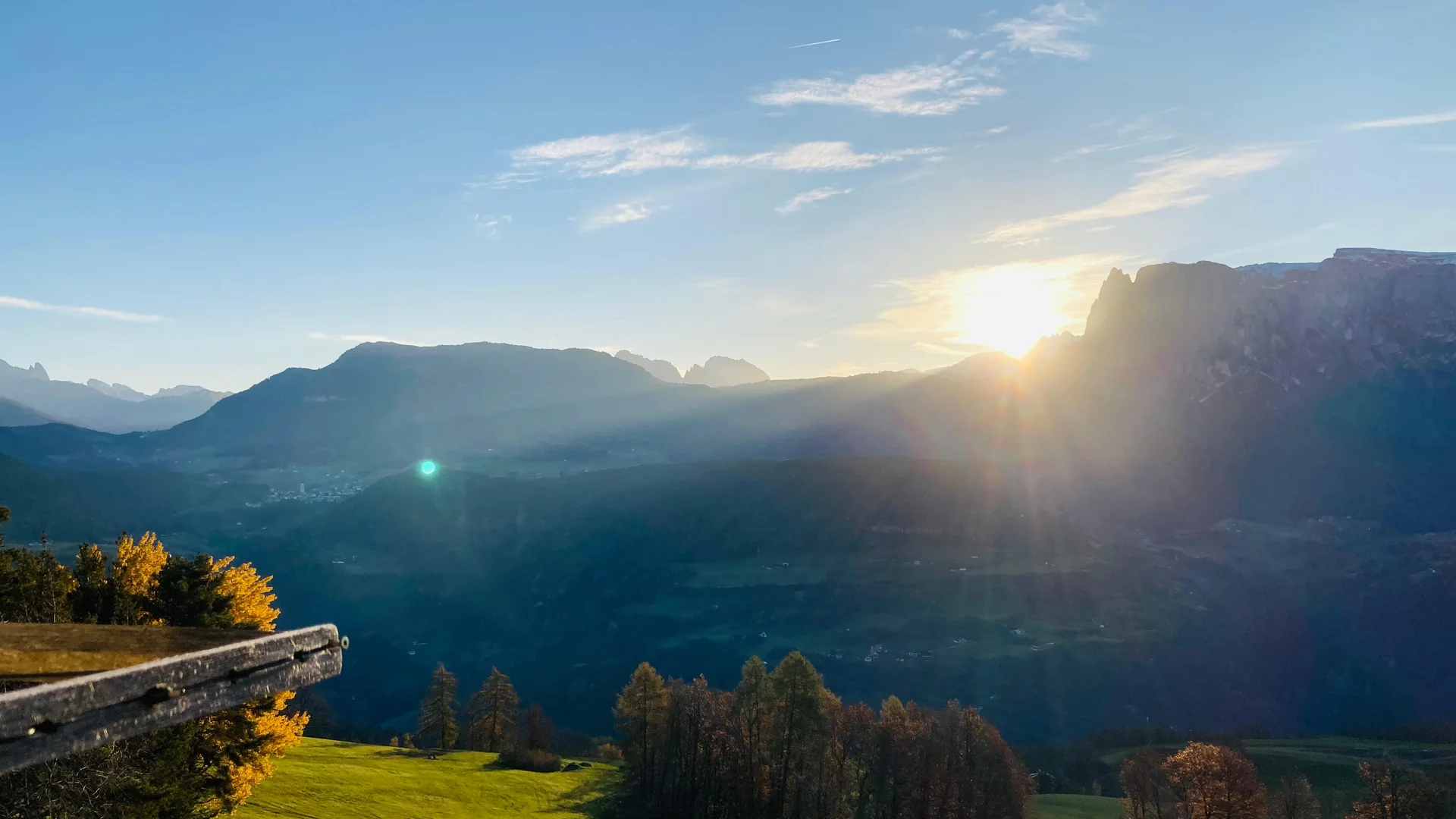Abendsonne über einem Bergtal mit grünen Wiesen und Holzzaun