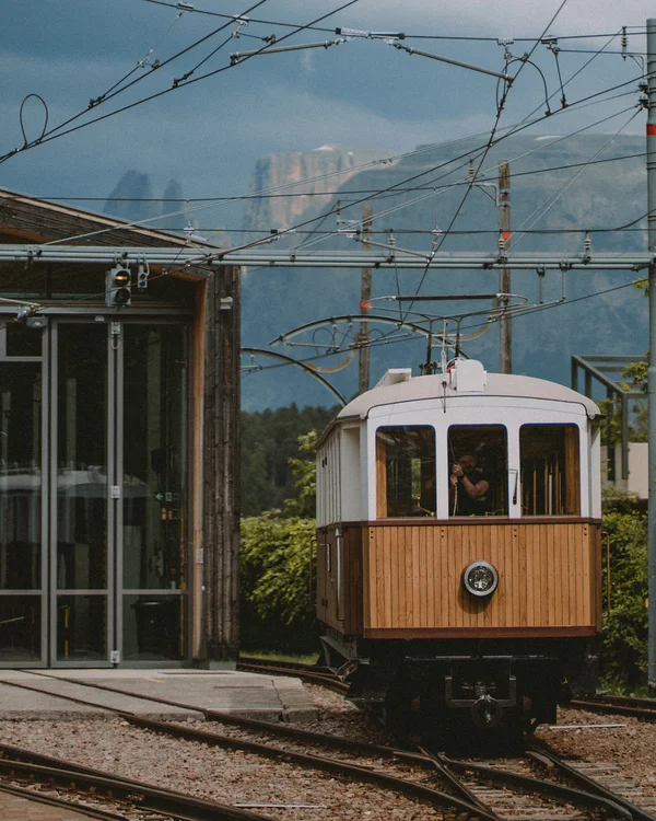 Vintage tram with a wooden front at a station, with mountains in the background