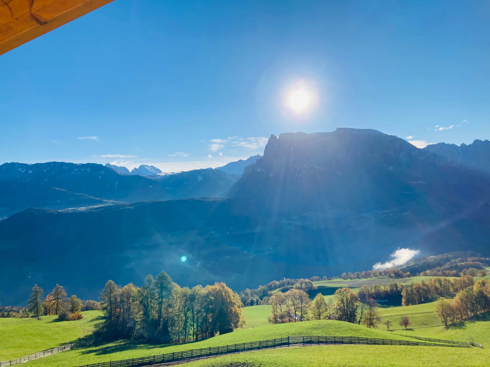 Sonnige Aussicht auf alpine Berge über grünen Wiesen und einem Holzzaun