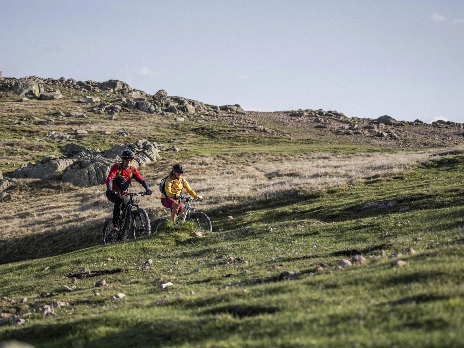 Urlaub am Ritten: die Insider-Tipps des Armonia Zwei Mountainbiker fahren über eine felsige, grasbewachsene Hügellandschaft