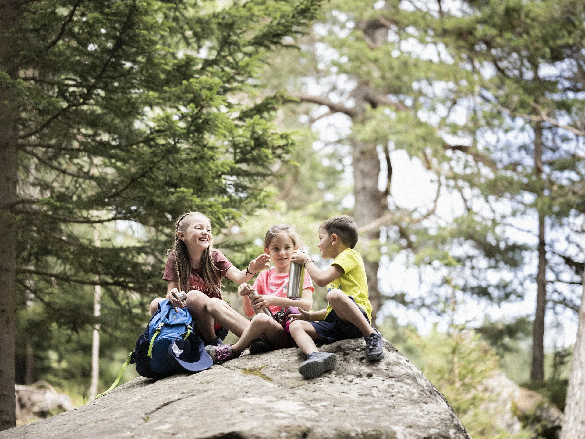 Urlaub am Ritten: die Insider-Tipps des Armonia Drei Kinder sitzen auf einem Felsen im Wald neben einem Rucksack