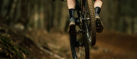 Mountainbiker fährt auf einem Waldweg über einen unebenen Trail