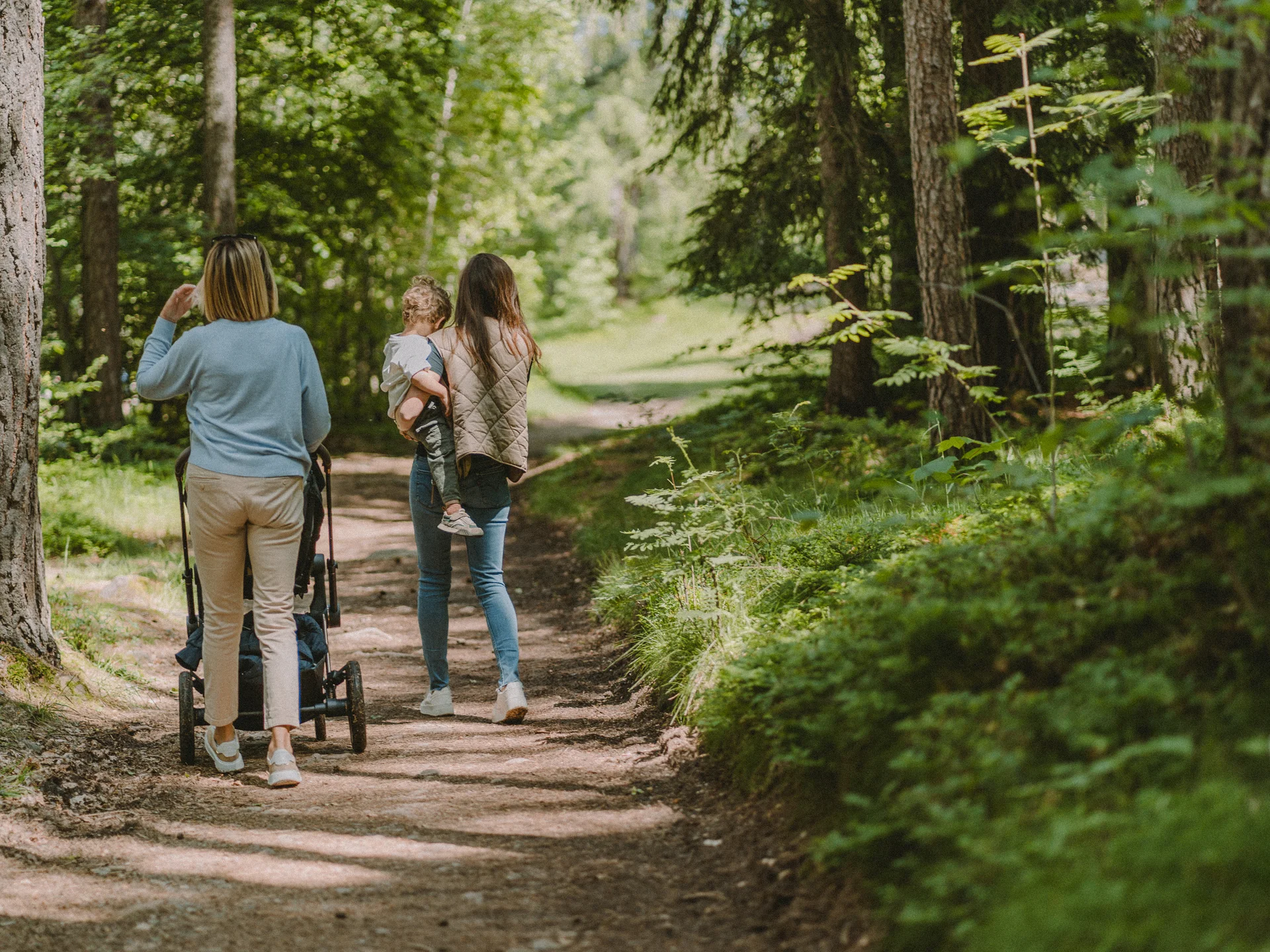 Urlaub am Ritten: die Insider-Tipps des Armonia Zwei Frauen gehen mit einem Kind und Kinderwagen auf einem Waldweg