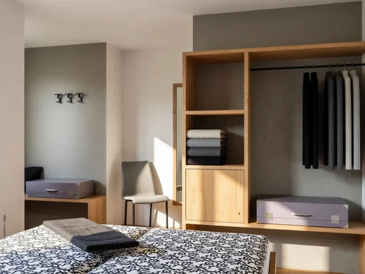 Ferienwohnung am Ritten: Armonia, Hof mit Musik Schlafzimmer mit gemustertem Bett, offenem Holzschrank, Kleidung und gefalteten Handtüchern