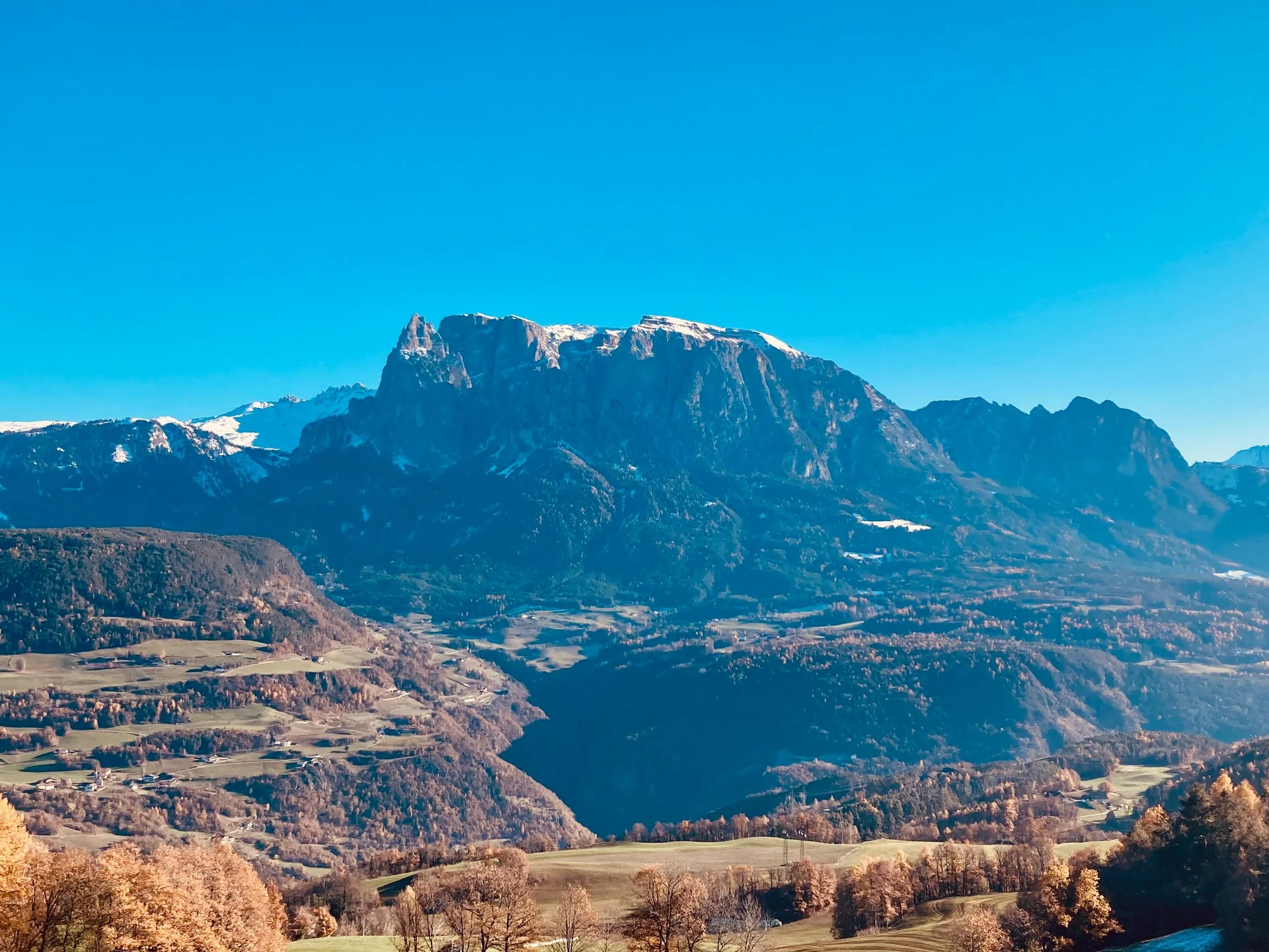 Blick auf ein herbstliches Tal und schneebedeckte Berge unter blauem Himmel