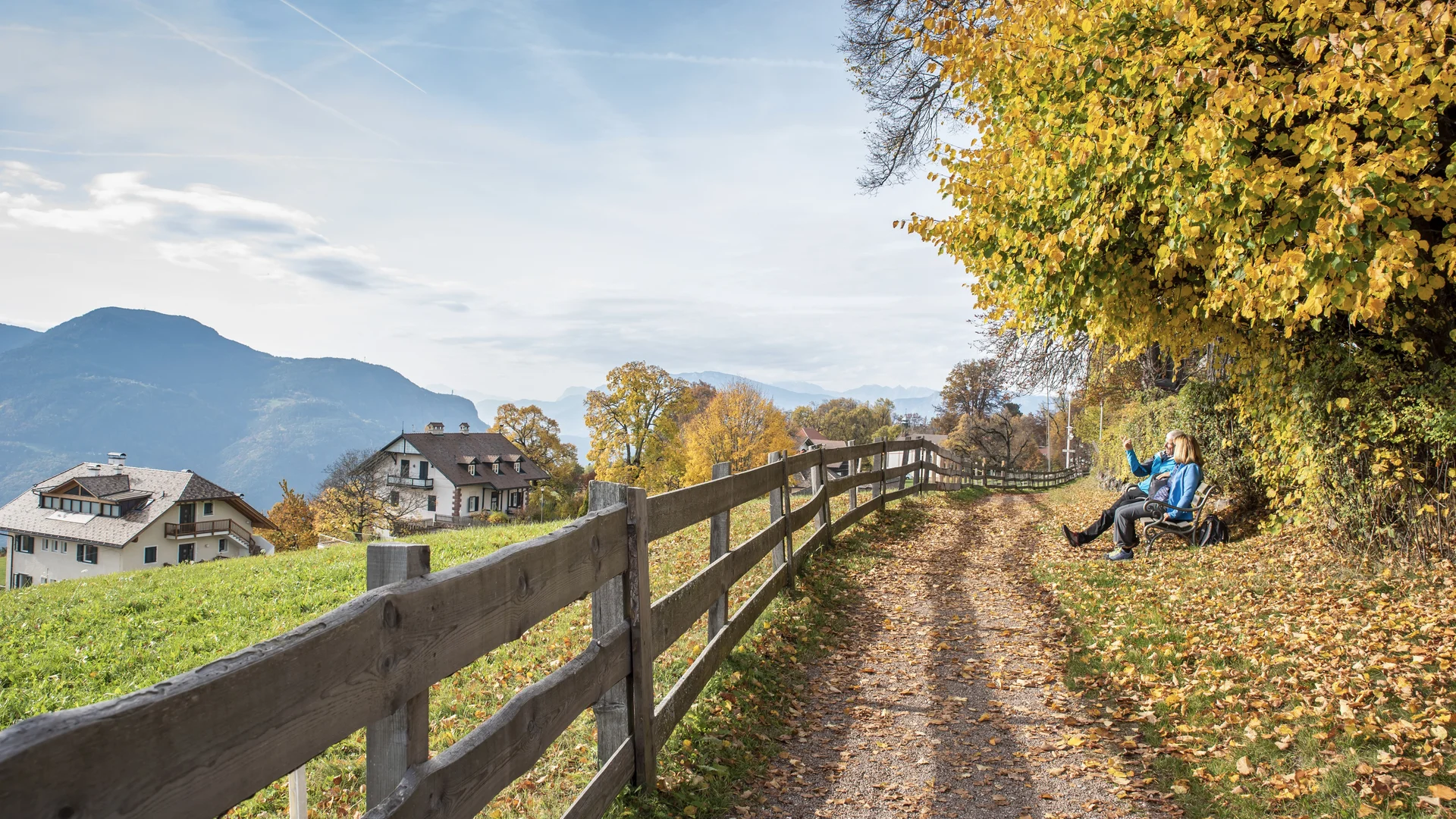 Bilder vom Armonia: Hof am Ritten in Südtirol Herbstlicher Weg mit Holzzaun, Bergblick und zwei Menschen auf einer Bank