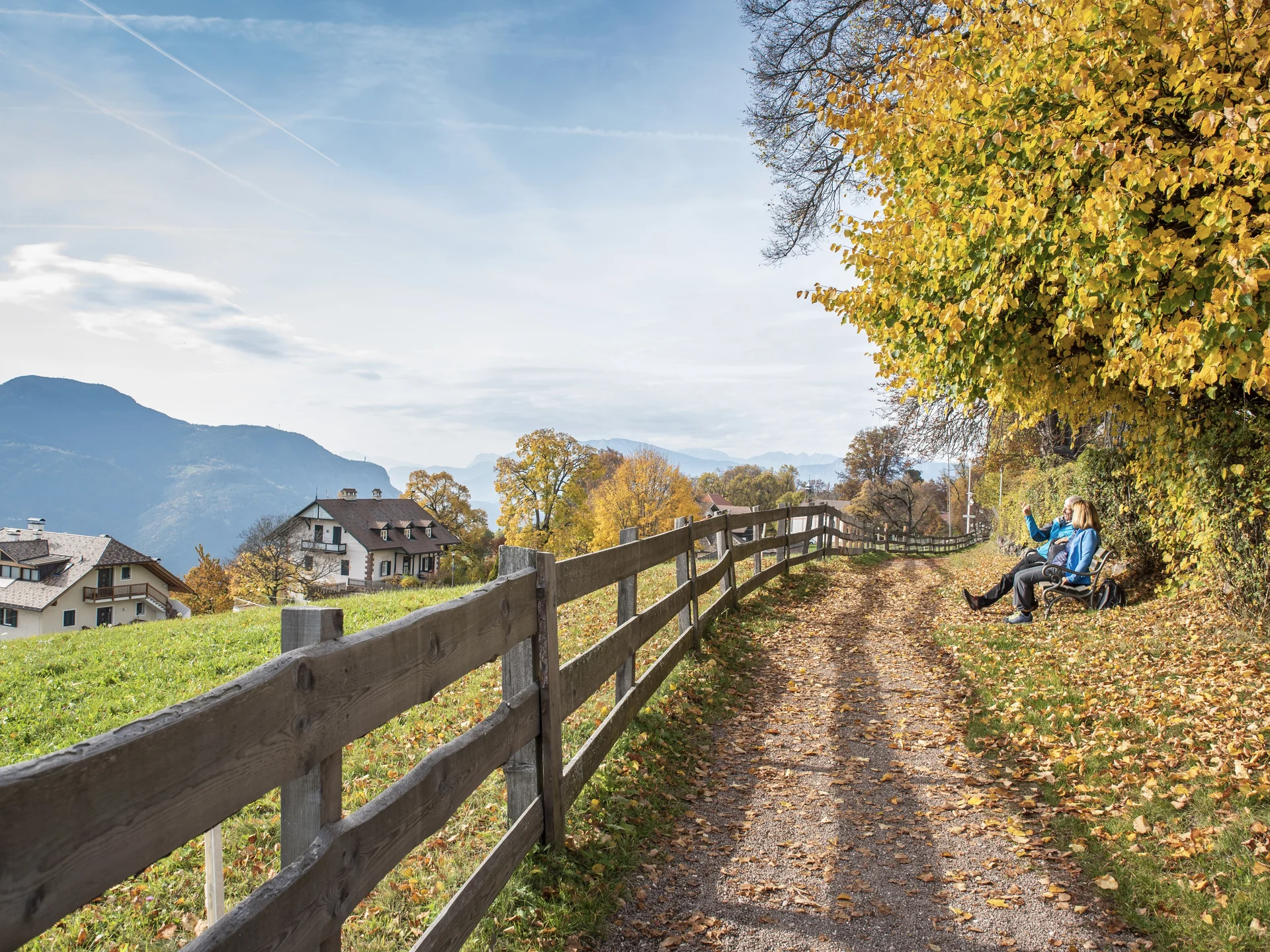 Urlaub am Ritten: die Insider-Tipps des Armonia Herbstlicher Weg mit Holzzaun, Bergblick und zwei Menschen auf einer Bank