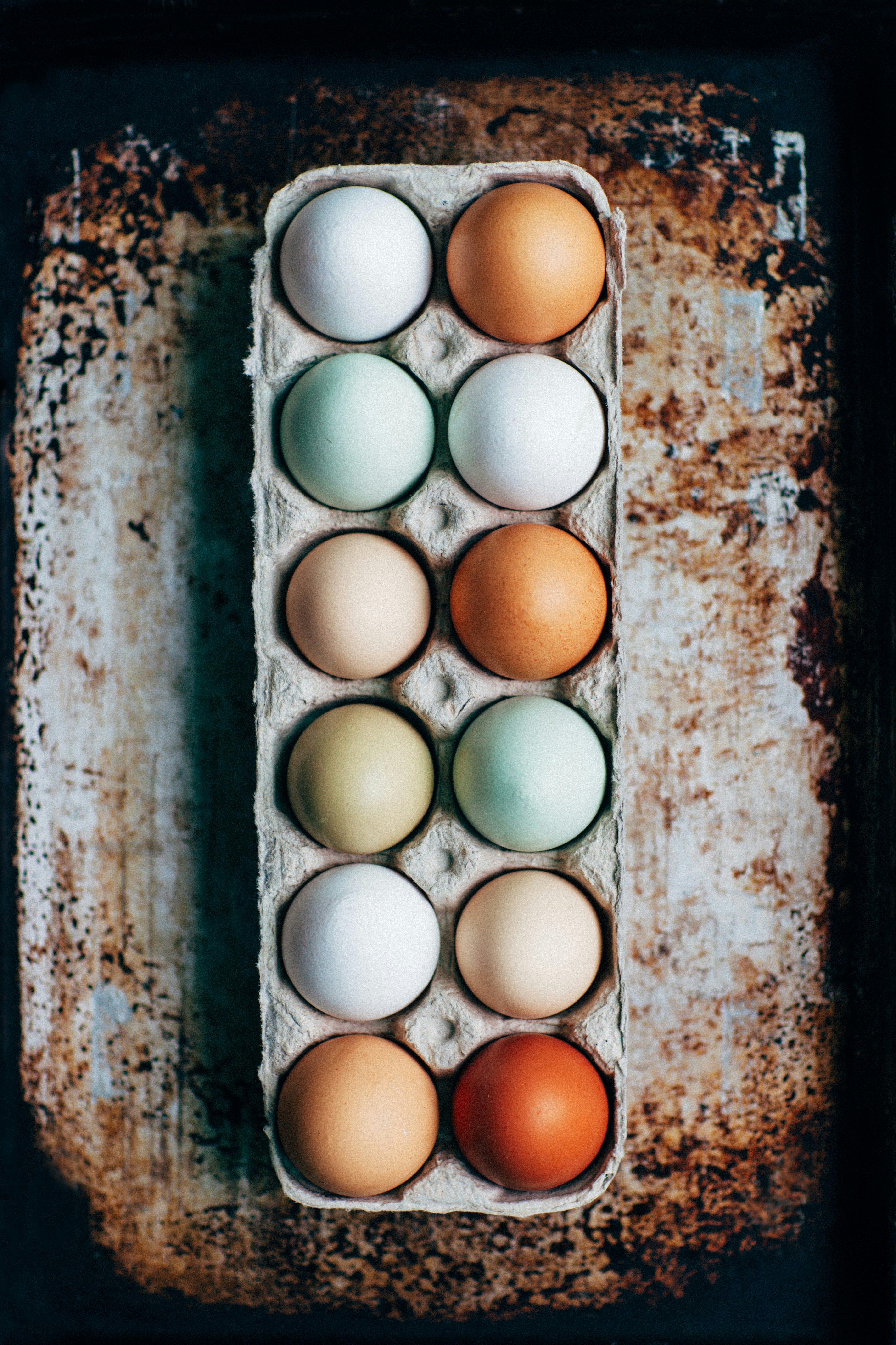 Top view of twelve colorful eggs in an egg carton on a rustic surface